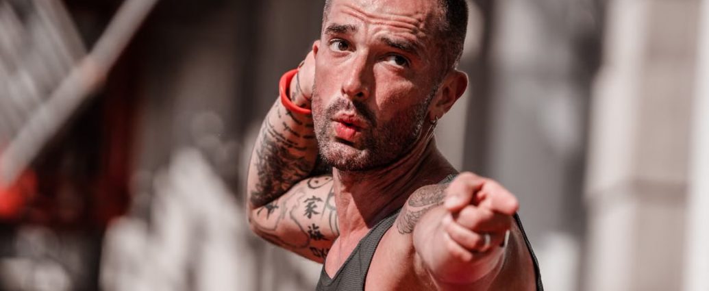 Tattooed man in a tank top points with focus during outdoor fitness activity in A Coruña.